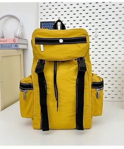 Detail of a yellow nylon backpack featuring buckle straps and multiple zipper pockets