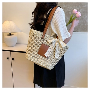Detail of a beige woven straw tote bag with brown leather straps and white lace bow accessory