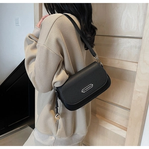 Détail du sac à main en cuir noir gaufré lézard avec logo argenté et pendentif en métal