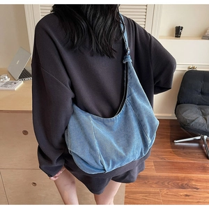 Detail of a large blue denim crescent hobo bag worn by a model in a cozy home office setting