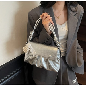 Détail du sac à main argenté plissé avec nœud, breloque perle et ruban de dentelle
