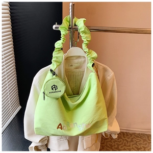 Détail du sac cabas plissé vert néon avec une mini pochette ronde amovible sur un blazer blanc