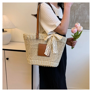 Detail view of woven straw tote bag with delicate lace bow and leather shoulder straps