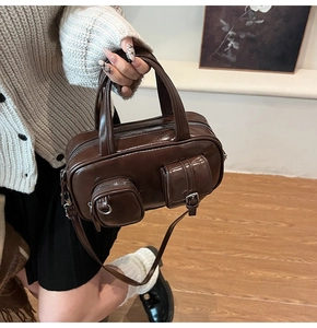 Detail of dark brown glossy crossbody bag featuring two functional front pockets and twin handles