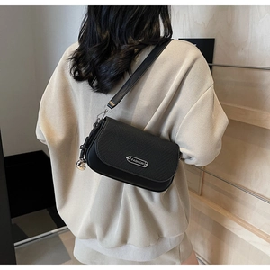 Détail d'un sac bandoulière noir avec rabat texturé et plaque métallique argentée FASHION