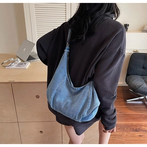 Blue denim hobo bag with adjustable strap shown on shoulder in a cozy interior setting