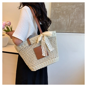 Detail view of woven straw tote bag featuring brown leather straps and lace bow decoration