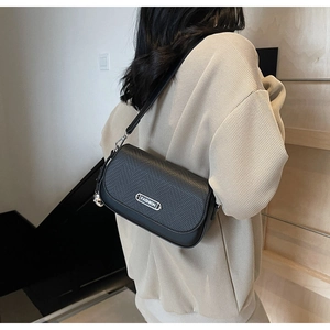Détail du sac à bandoulière noir avec rabat texturé et plaque en métal argenté