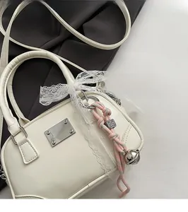 Detail der weißen Boston-Tasche mit Spitzenschleife, Webanhänger und Metallplakette