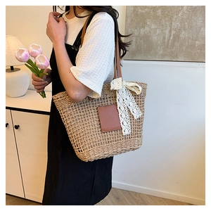 Detail of woven straw tote bag featuring brown leather patch and delicate white lace ribbon