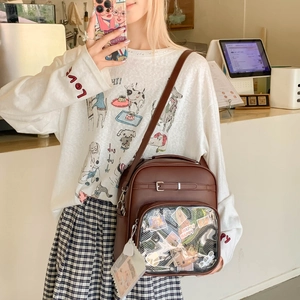 Détail du sac Ita en cuir marron foncé avec fenêtre transparente et badges décoratifs