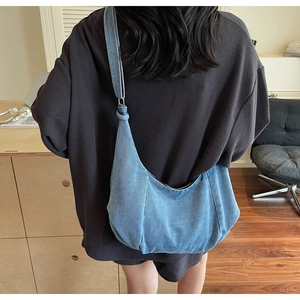Detail shot of a large blue denim hobo bag with adjustable strap worn by a model