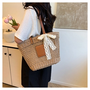 Detail of woven straw tote bag featuring leather handles and a white lace bow accent