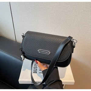 Détail du sac bandoulière noir avec rabat tissé et pendentif en forme de cœur argenté
