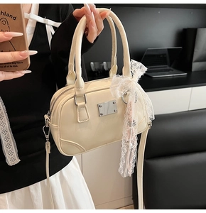 Detail der cremefarbenen Bowling-Tasche mit Glanzeffekt und weißem Spitzenbogen-Anhänger