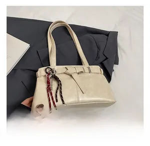 Close-up of creamy white underarm bag with decorative buckle and woven pendant details