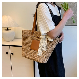 Close-up of woven straw tote bag featuring brown leather straps and a white lace bow detail