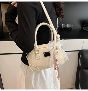 Detail der cremeweißen Ledertasche mit Spitzen-Schleife und geflochtenem Anhänger