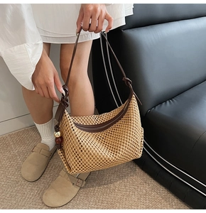 Détail du sac à bandoulière tissé beige avec bandoulière en cuir brun et pompon en perles