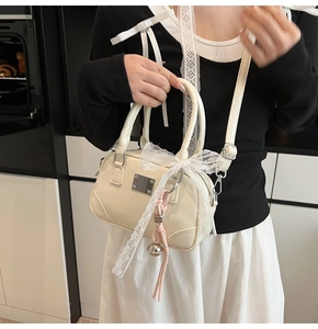 Detail der cremefarbenen Boston-Tasche mit Spitzenschleife und silbernem Glockenanhänger