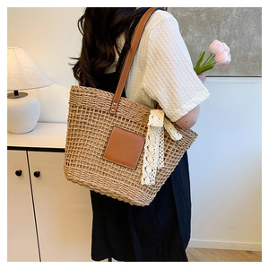 Detail of woven straw tote bag featuring leather patch and elegant lace ribbon detail