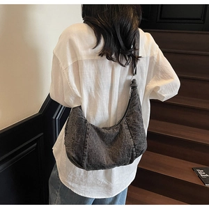 Black washed denim crescent bag with wide strap shown on model in vintage setting