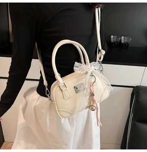 Detailansicht der cremefarbenen Kunstledertasche mit Spitzenschleife und Anhänger