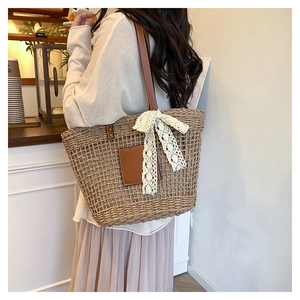 Detailed side view of woven straw tote bag with leather strap and white lace bow