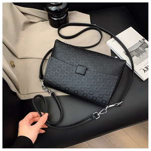 Detail of black embossed square shoulder bag with elegant flap buckle on fabric background
