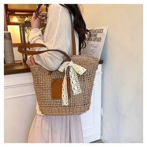 Detail of woven straw tote bag with brown leather handles and lace bow on a shoulder strap