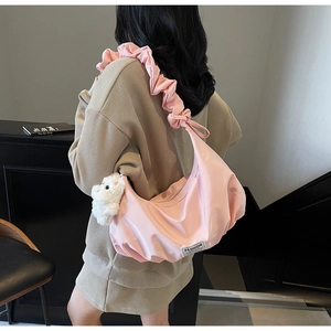 Detailed close-up of pink crescent shoulder bag with pleated strap and teddy bear charm