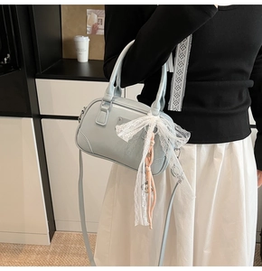 Detailansicht der hellblauen Lackhandtasche mit Spitzenschleife und Anhänger am Model