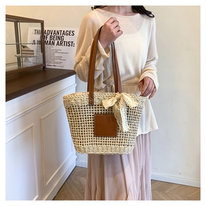 Detail of woven straw tote bag featuring brown leather handles and a lace bow tie accent