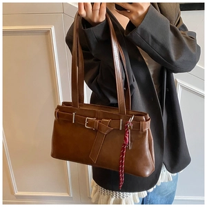 Detail of dark brown retro shoulder bag with metallic buckle and woven pendant on model