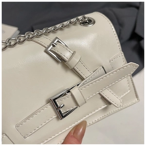 Close-up of cream white PU leather texture with silver buckles and chain on a shoulder bag
