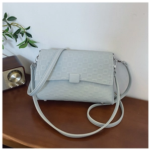 Detail of light blue faux leather underarm bag with geometric embossed texture on a wooden table