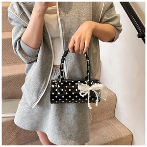 Détail d'un sac cylindrique à pois noirs avec nœud en dentelle et breloque en perles