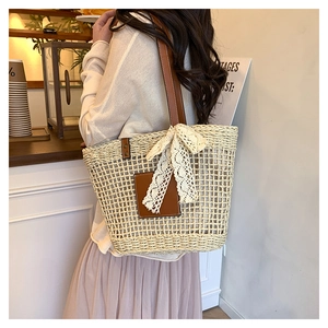 Detail of woven straw tote bag featuring brown leather straps and a delicate lace bow