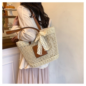 Detail of beige straw tote bag with brown leather straps and lace bow decoration