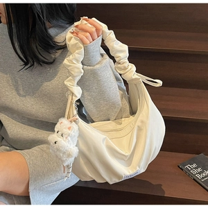 Detail view of cream hobo bag featuring pleated fabric and cute white plush puppy charm