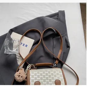 Détail du sac bandoulière étanche avec poignées en cuir marron et breloque ours