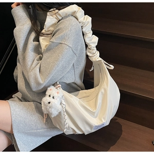 Detail of creamy white crescent bag featuring pleated shoulder strap and plush puppy charm