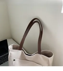 Detail of canvas tote bag with brown leather strap and laptop in office setting