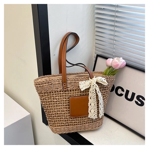 Detail of woven straw tote bag with brown leather handles and a white lace bow decoration