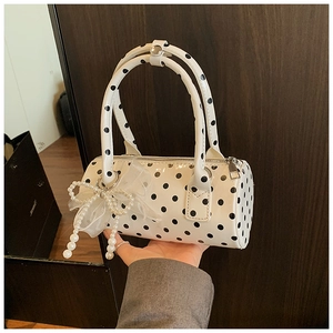 Détail d'un sac cylindrique blanc à pois avec noeud en dentelle et perles