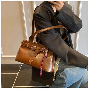 Detail view of brown leather underarm bag with decorative belt buckle and keychain charm