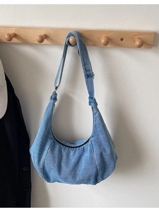 Blue denim half-moon hobo bag with adjustable strap hanging on a wooden hook