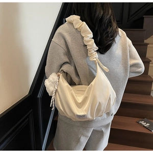 Detail of a beige pleated scrunchie shoulder bag with a plush pompom and fashion tag