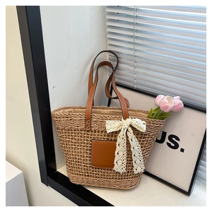 Detail of hand-woven straw tote bag with brown leather patch and white lace bow