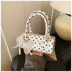 Gros plan du sac cylindrique blanc à pois avec breloque nœud en perles et doubles poignées